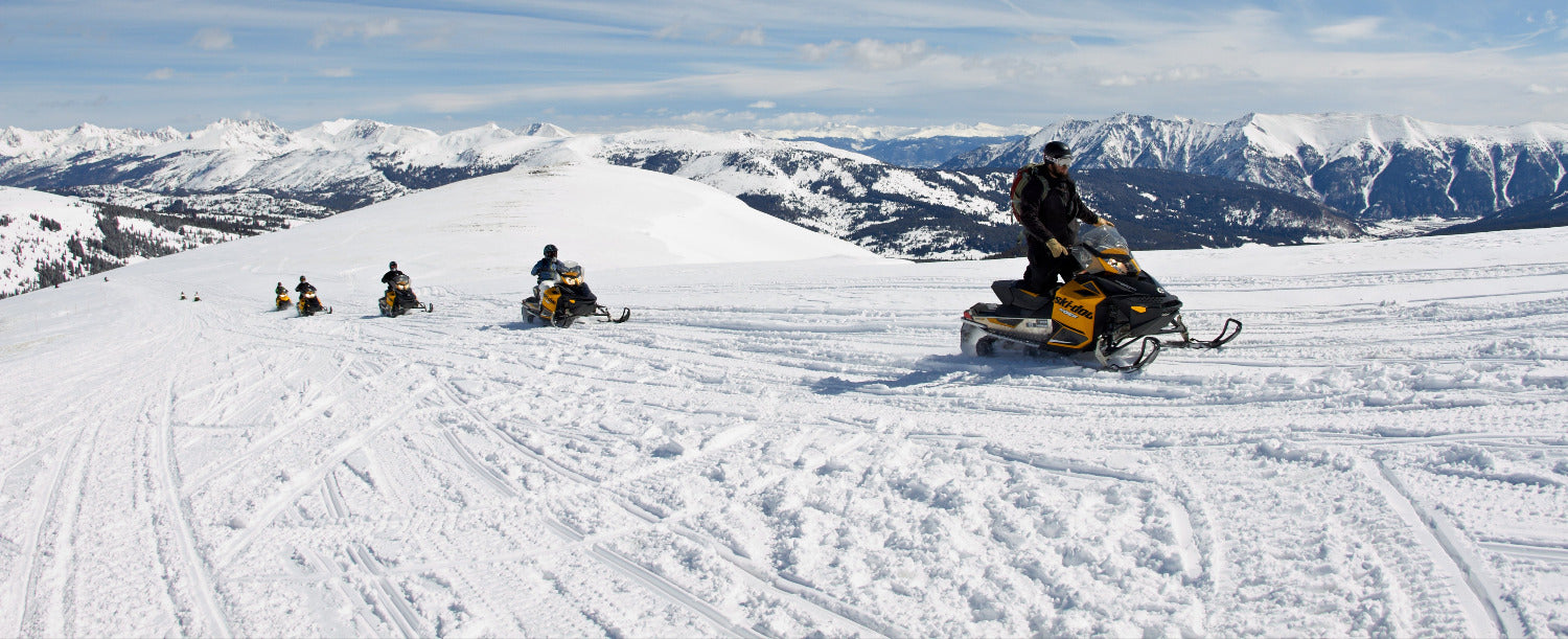 People on snowmobiles in a snowy landscape with mountains in the background